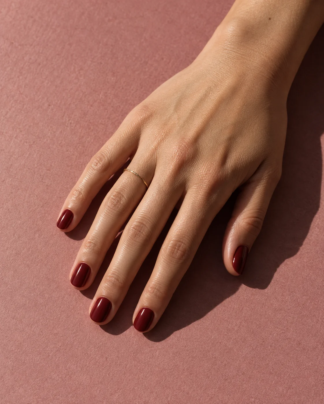 Illustrative short oval manicure in glossy dark cherry red on dusty rose paper